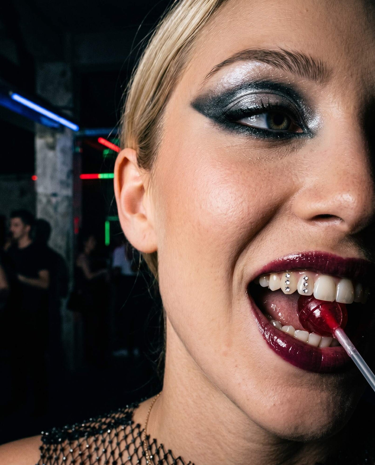 Blonde avec sucette et strass dentaire, maquillage argenté en club